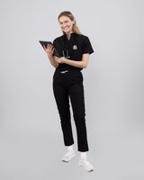 Junge Ärztin in medizinischer Berufsbekleidung in schwarz lächelt in die Kamera