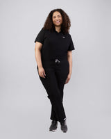 Junge Ärztin in Sneakern und moderner medizinischer Damenhose in schwarz