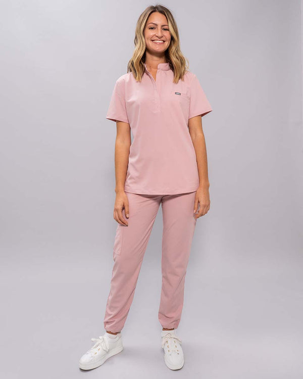 Junge Ärztin in weißen Sneakern und moderner Arbeitsbekleidung in rosa