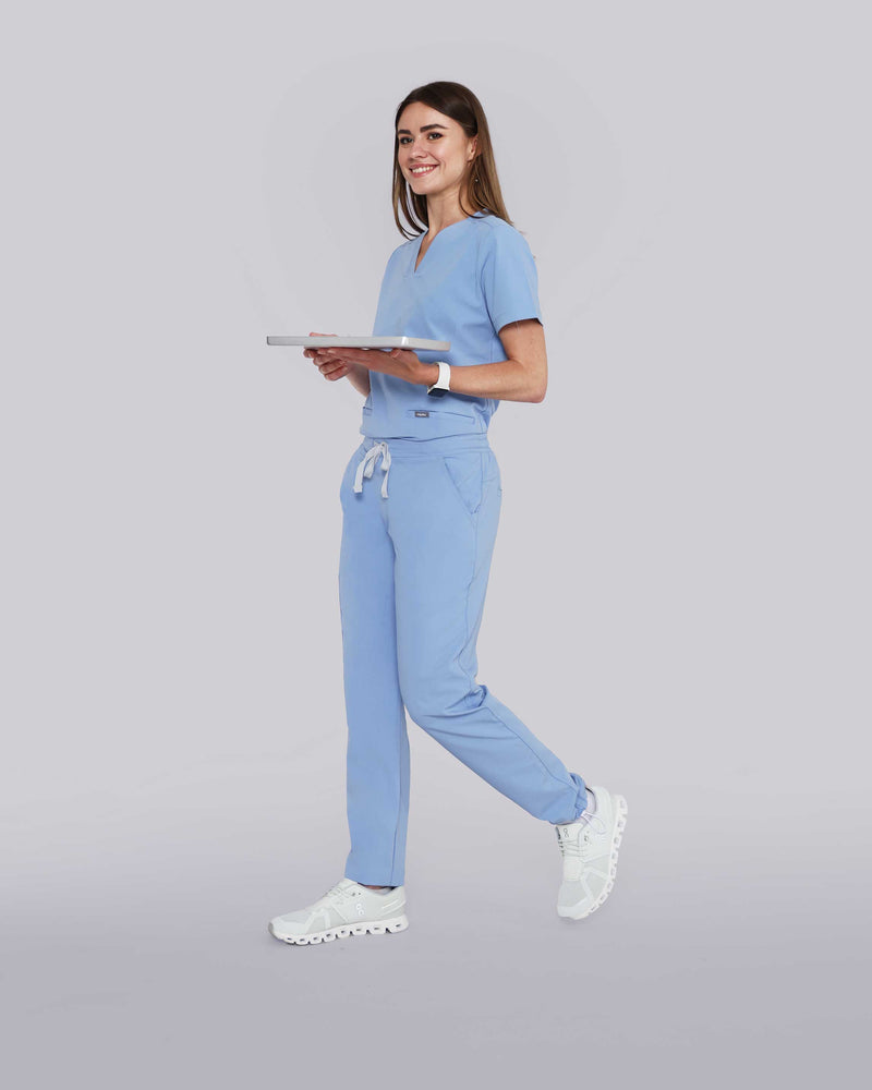 Junge Ärztin in medizinischer Berufsbekleidung in hellblau lächelt in die Kamera