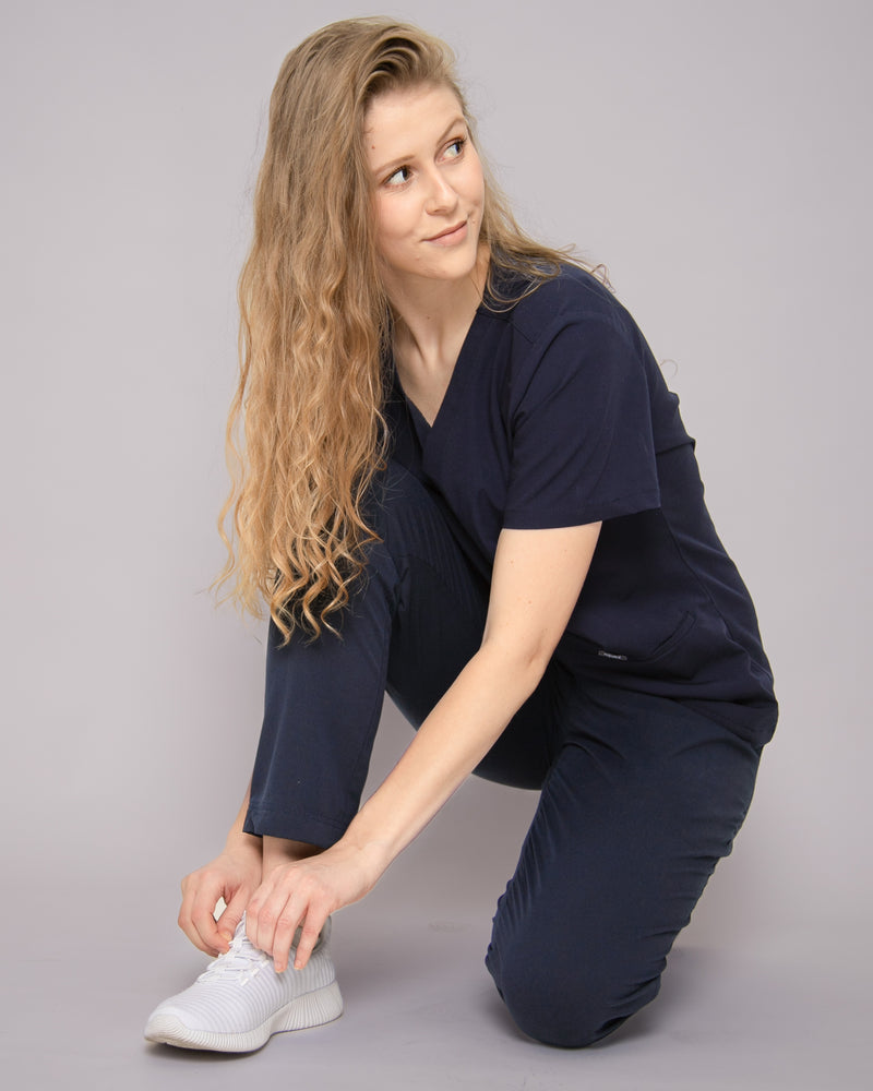 Junge Ärztin mit blonden Haaren bindet sich ihre Sneaker in dunkelblauer medizinischer Berufsbekleidung
