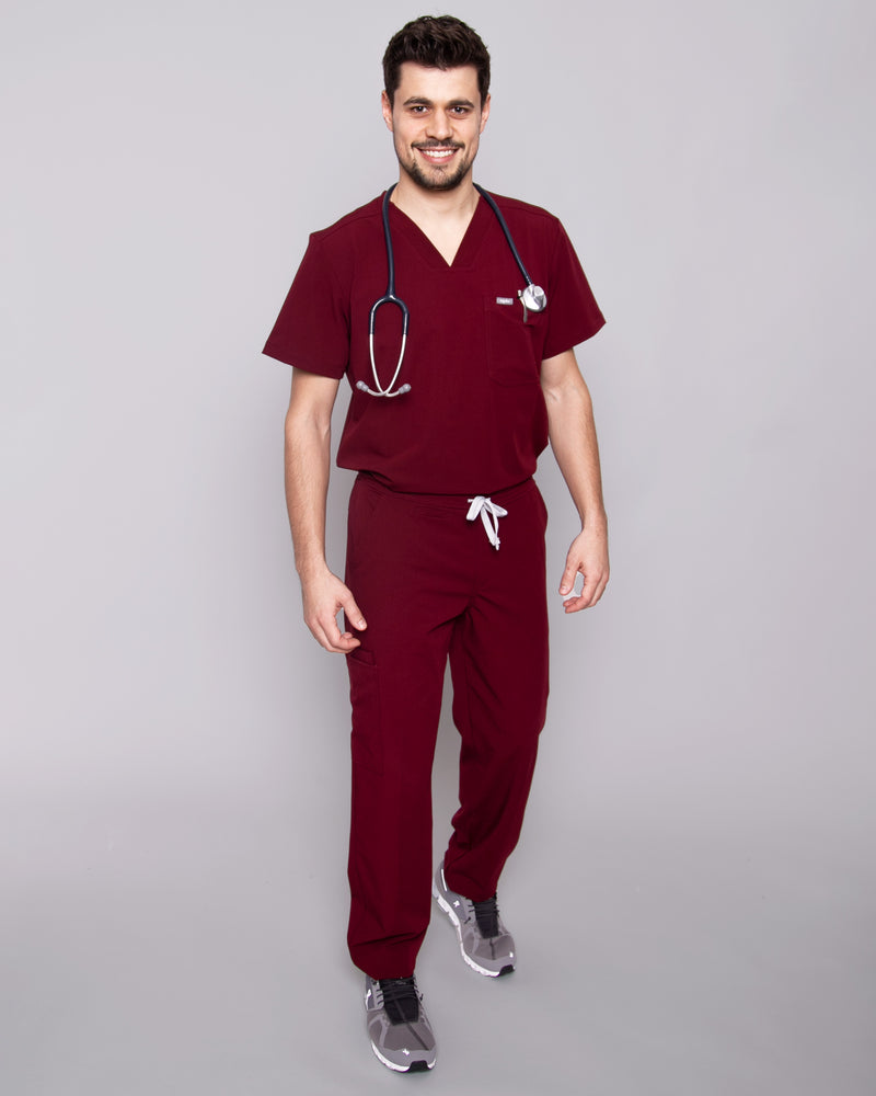 Junger Arzt mit moderner dunkelroter medizinischer Arbeitskleidung und Sneakern
