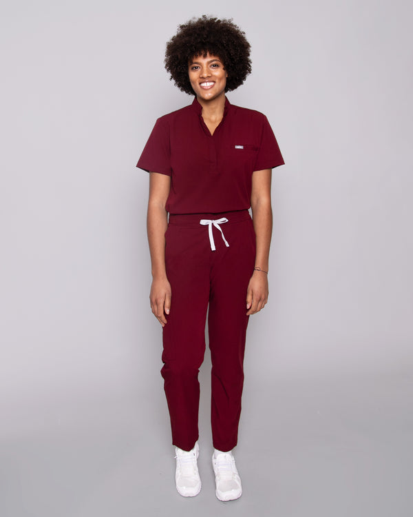 Junge Ärztin in weißen Sneakern und moderner Arbeitsbekleidung in dunkelrot
